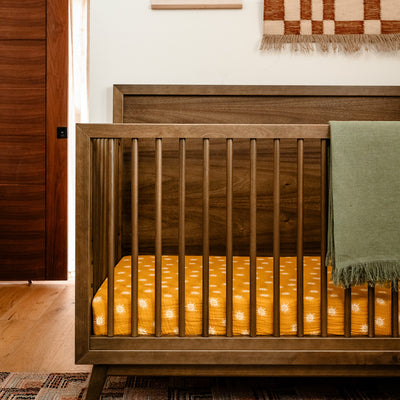 Closeup of Babyletto's Palma 4-in-1 Convertible Crib with green blanket over the rail  in -- Color_Natural Walnut