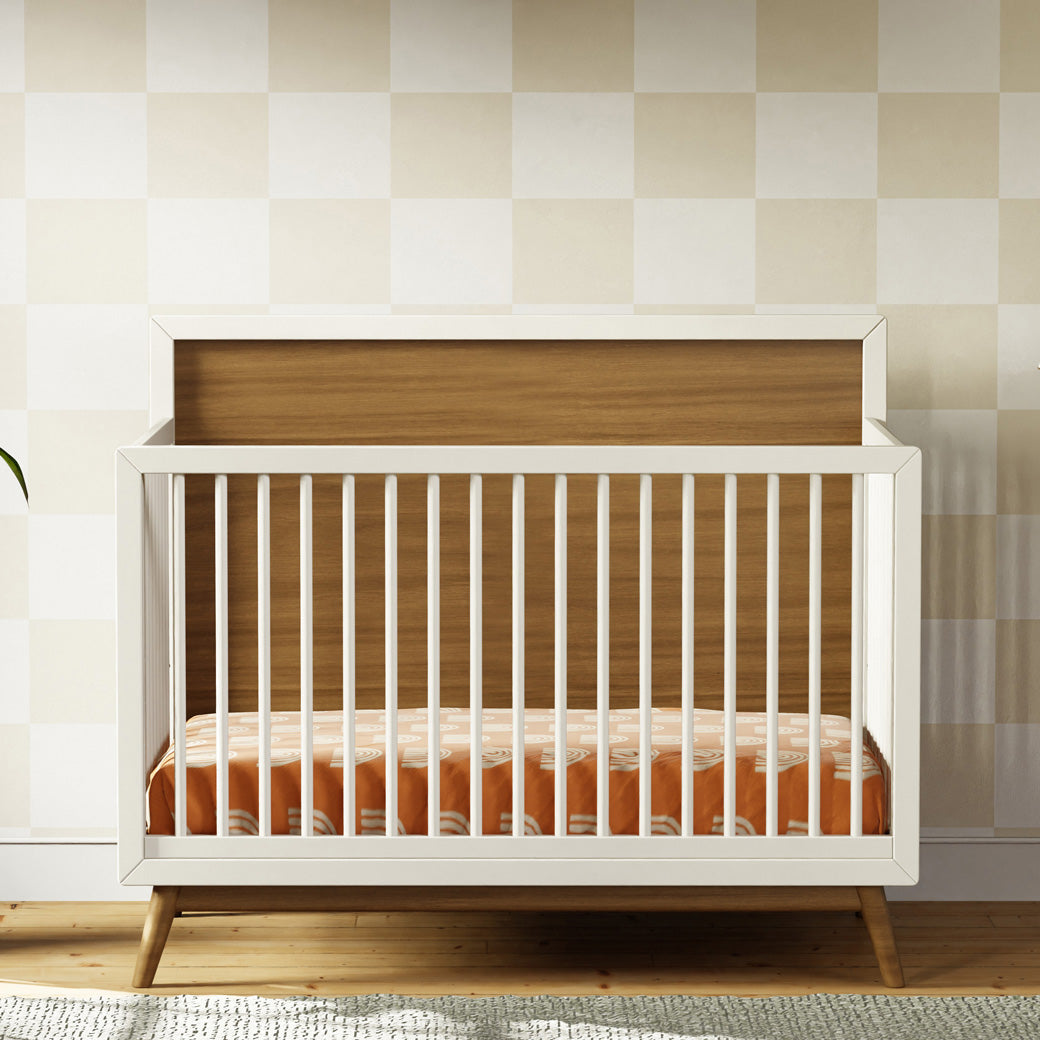 Front view of Babyletto's Palma 4-in-1 Convertible Crib in a tiled room in -- Color_Warm White with Natural Walnut