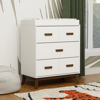 Babyletto's Scoot 3-Drawer Changer Dresser next to a window in -- Color_White/Natural Walnut