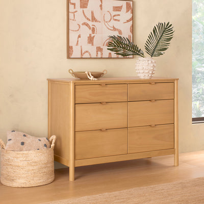 Babyletto Bondi 6-Drawer Dresser next to a basket and under a picture in -- Color_Honey