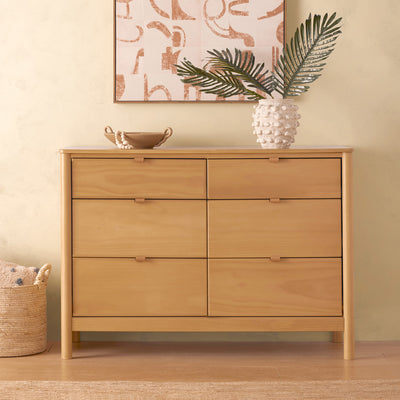 Front view of Babyletto Bondi 6-Drawer Dresser next to a basket and with a vase on top  in -- Color_Honey