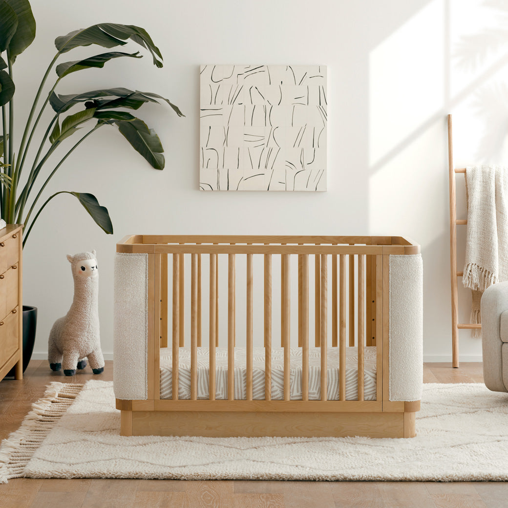 Front view of Babyletto Bondi Boucle 4-in-1 Convertible Crib next to a plant and lama toy in -- Color_Honey with Ivory Boucle