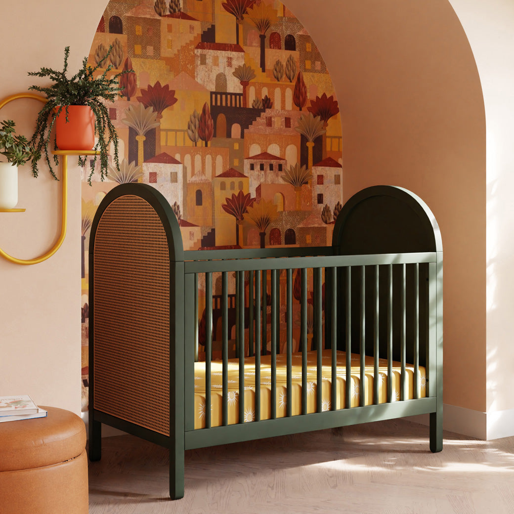 Babyletto Bondi Cane 3-in-1 Convertible Crib next to ottoman and shelf with plants in -- Color_Forest Green with Natural Cane