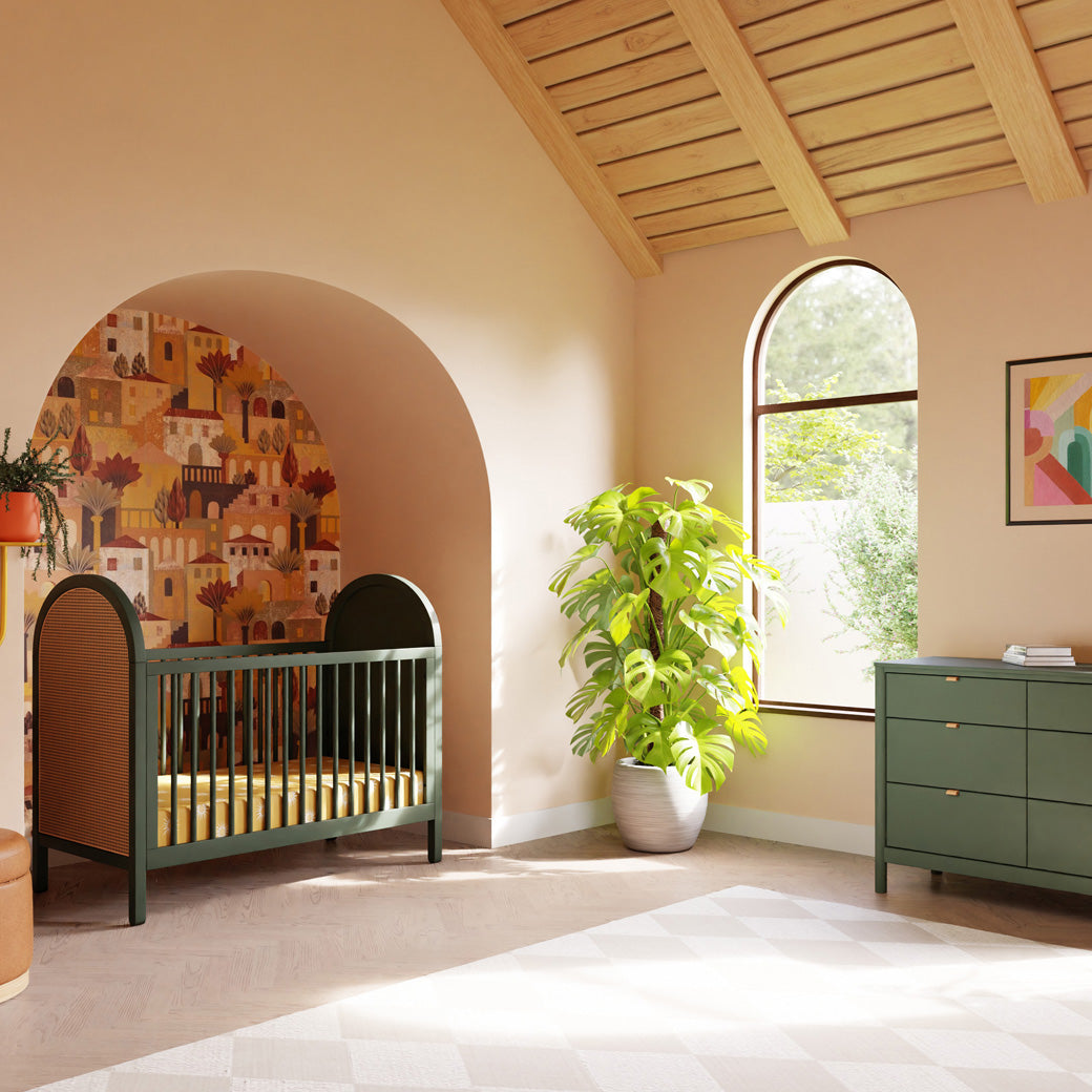 Babyletto Bondi Cane 3-in-1 Convertible Crib in a bright room next to a plant and window  in -- Color_Forest Green with Natural Cane