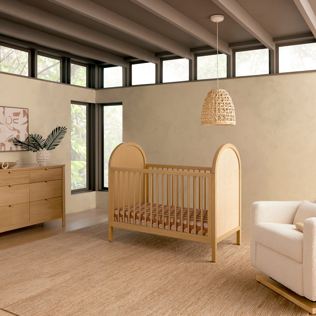 Babyletto Bondi Cane 3-in-1 Convertible Crib next to a recliner and dresser in -- Color_Honey with Natural Cane
