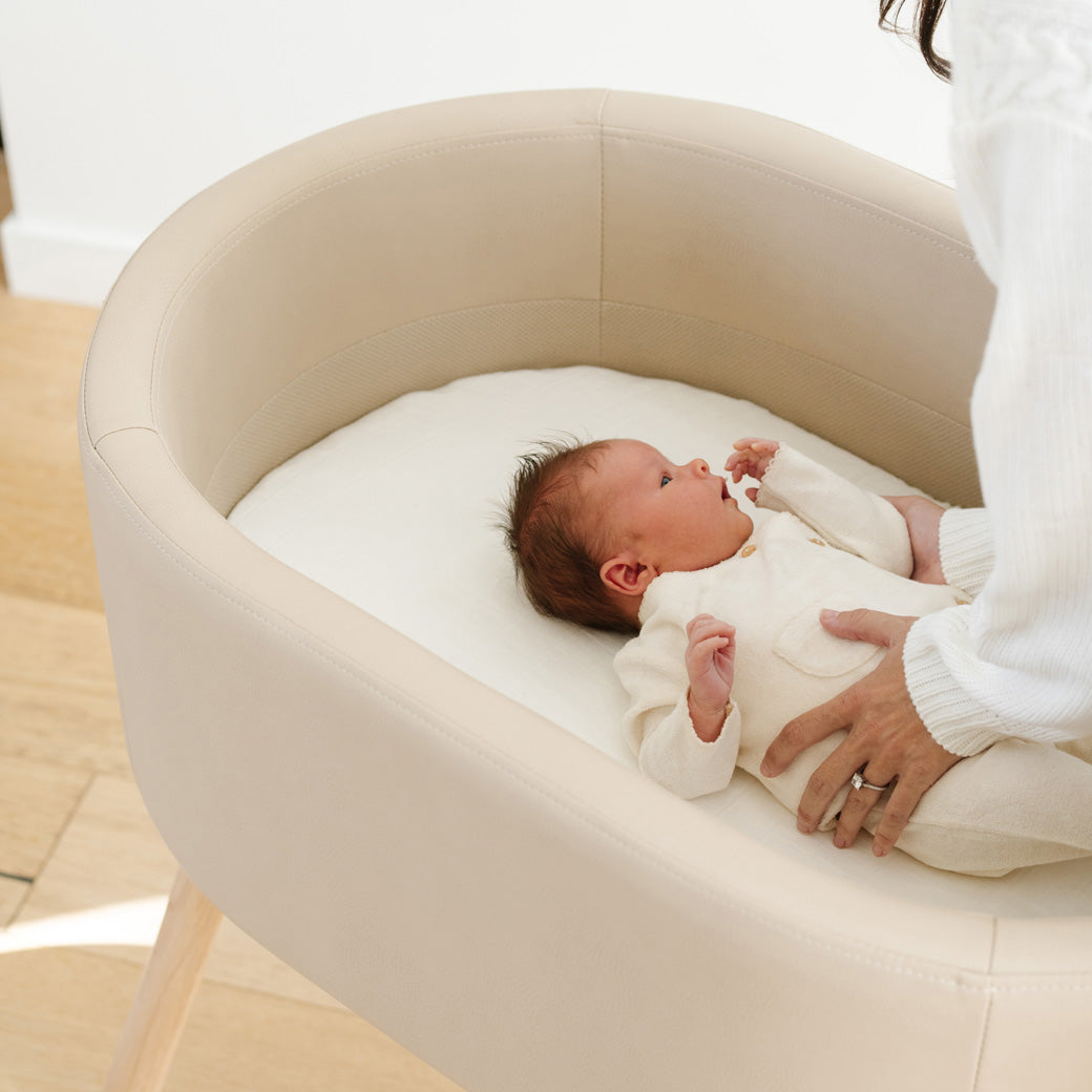 Mom placing baby in Babyletto GATHRE Capsule Bassinet in -- Color_Millet