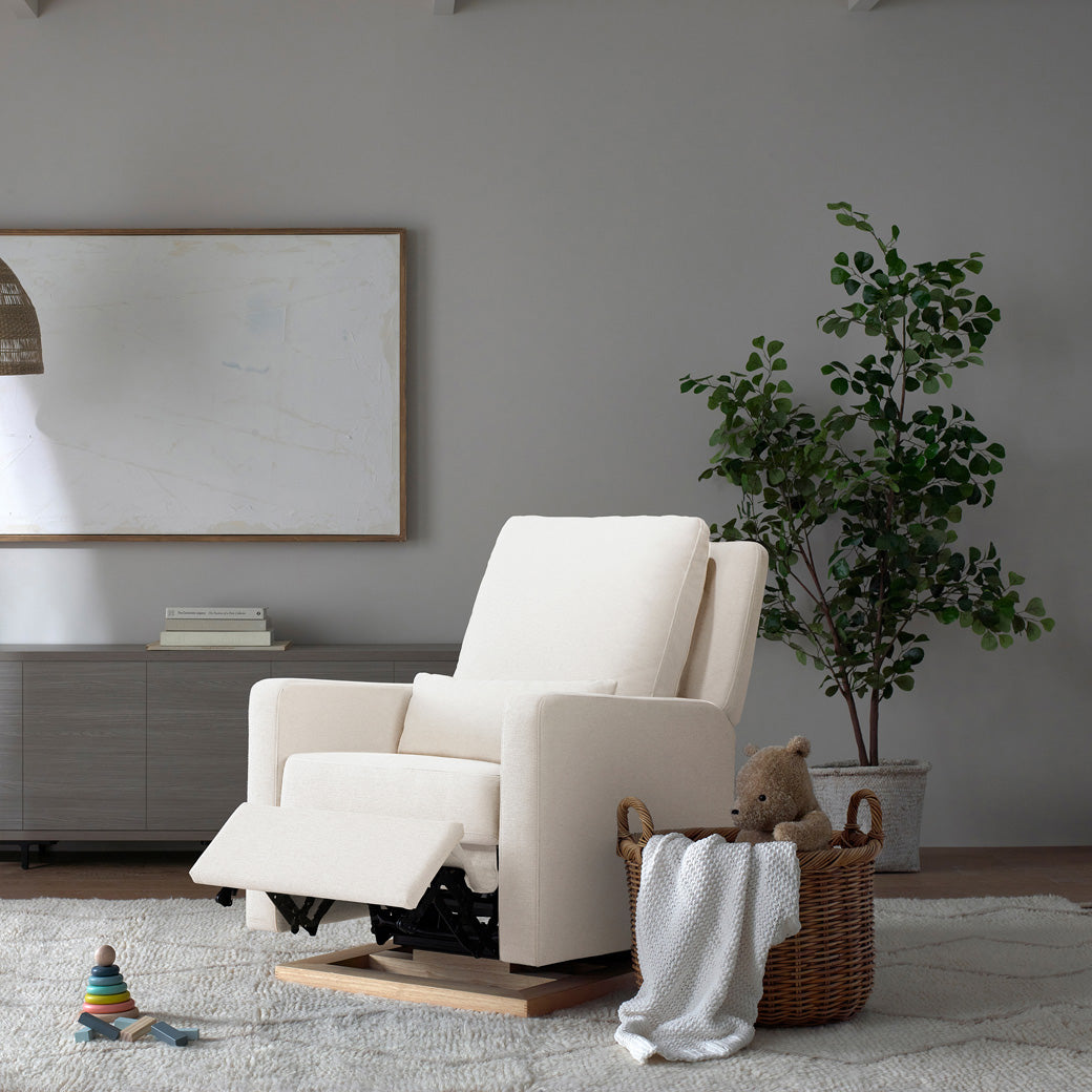 Reclined Babyletto Sigi Glider Recliner next to a basket  in -- Color_Performance Cream Eco-Weave with Light Wood Base