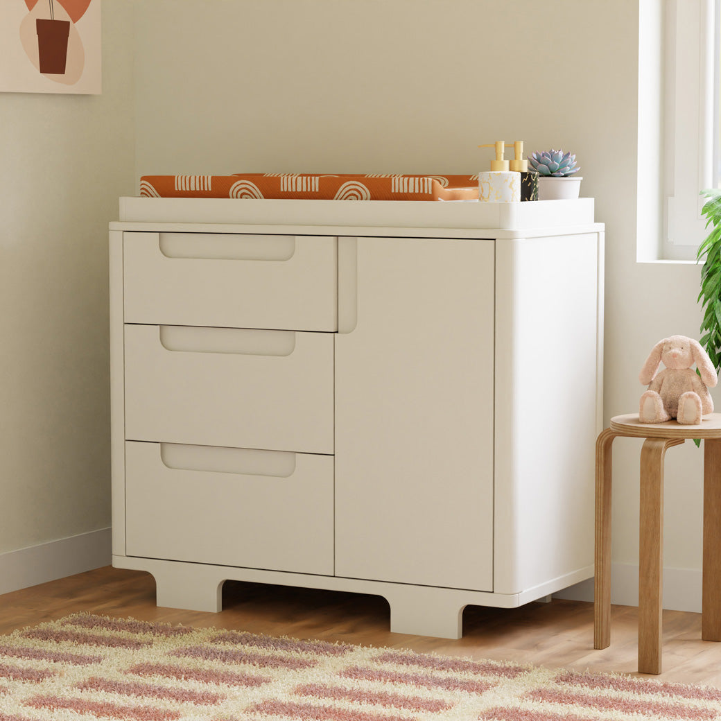 Babyletto Yuzu 3-Drawer Changer Dresser  with changing tray next to a stool in -- Color_White