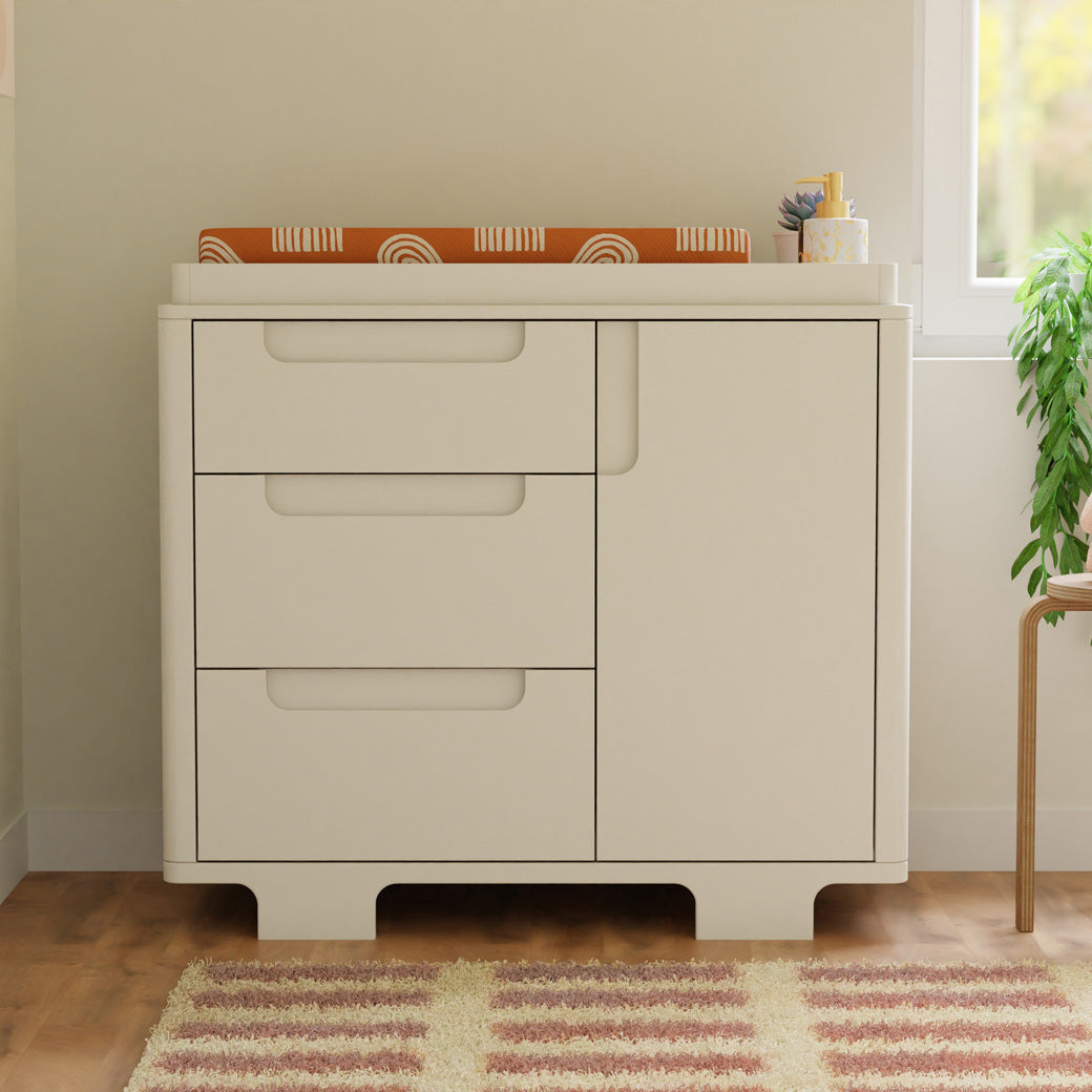 Front view of Babyletto Yuzu 3-Drawer Changer Dresser with changing tray next to a window and stool in -- Color_White