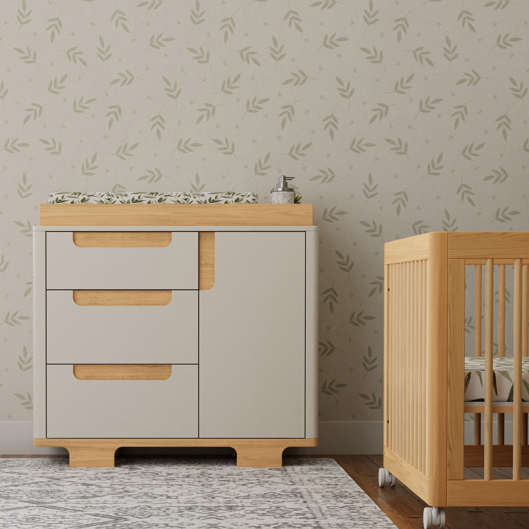 Front view of Babyletto Yuzu 3-Drawer Changer Dresser next to a crib in -- Color_White / Natural