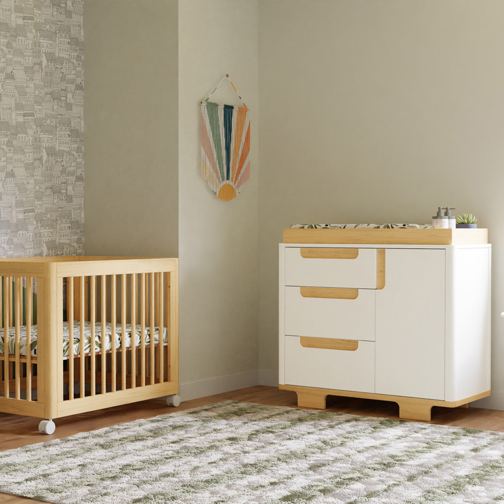 Babyletto Yuzu 3-Drawer Changer Dresser next to a natural crib in -- Color_White / Natural