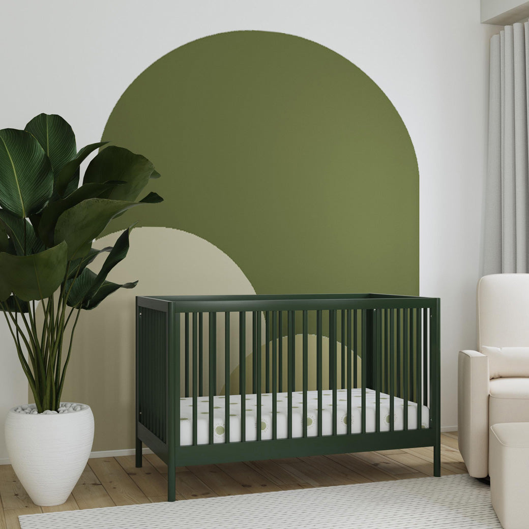 DaVinci Birdie 3-in-1 Convertible Crib next to a plant and a recliner  in -- Color_Forest Green