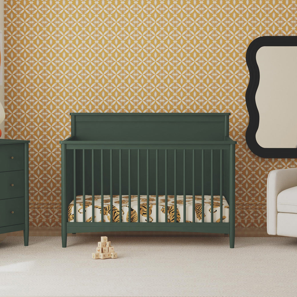 Front view of DaVinci Frem 4-in-1 Convertible Crib next to dresser and recliner  in -- Color_Forest Green