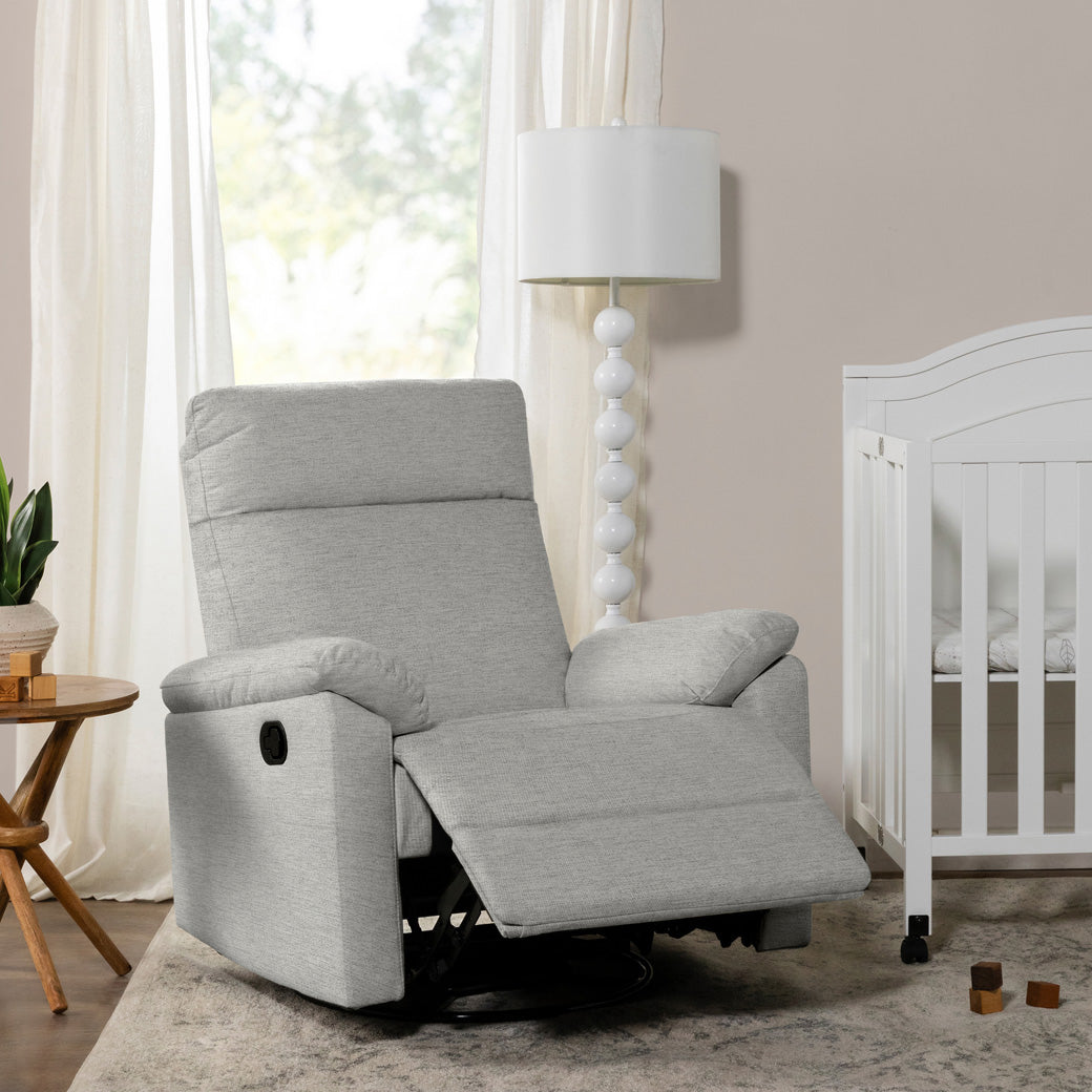 DaVinci Suzy Recliner and Swivel Glider with footrest up and next to a crib  in -- Color_Frost Grey