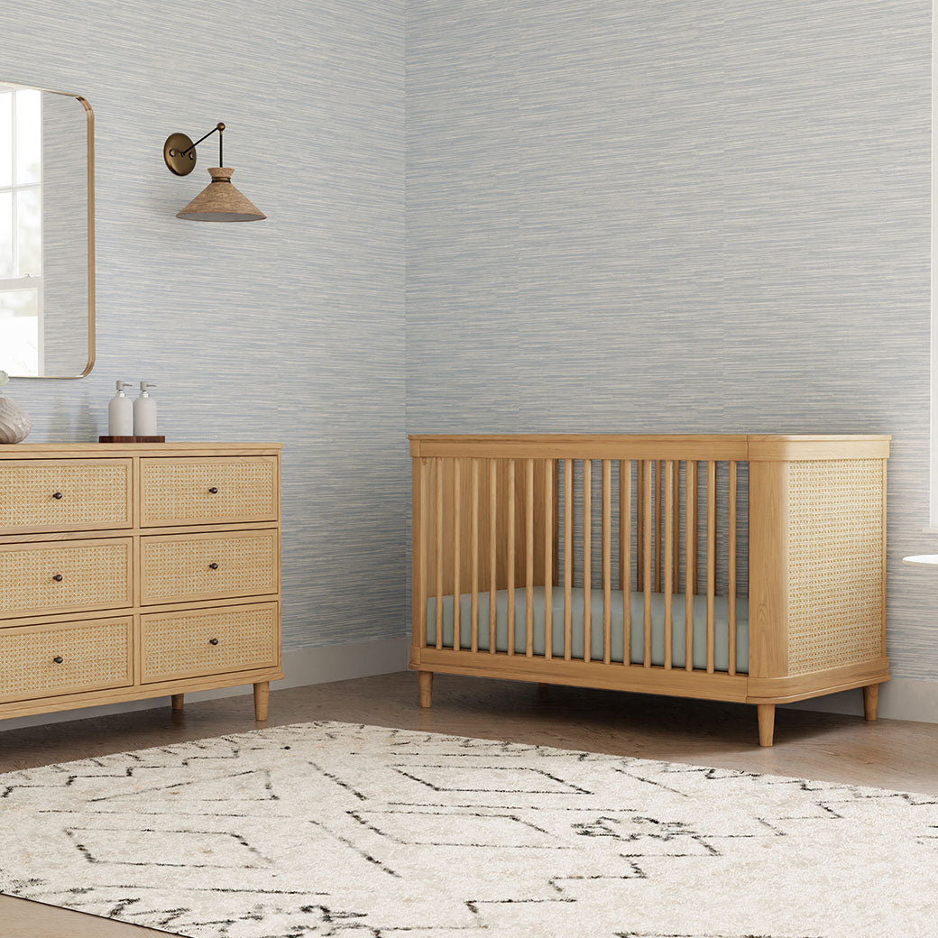 The Namesake Marin 3-in-1 Convertible Crib next to a dresser in -- Color_Honey/Honey Cane