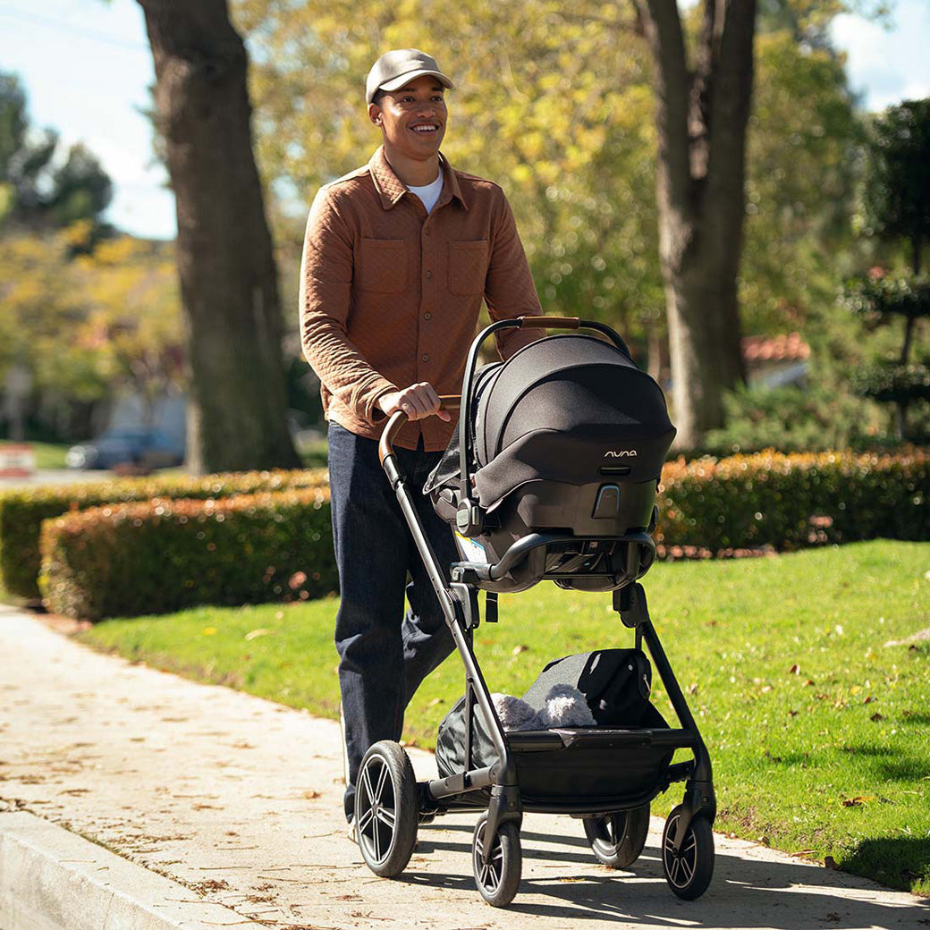 Dad pushing baby in  Nuna PIPA Aire Infant Car Seat + PIPA Series Base on stroller in -- Color_Caviar
