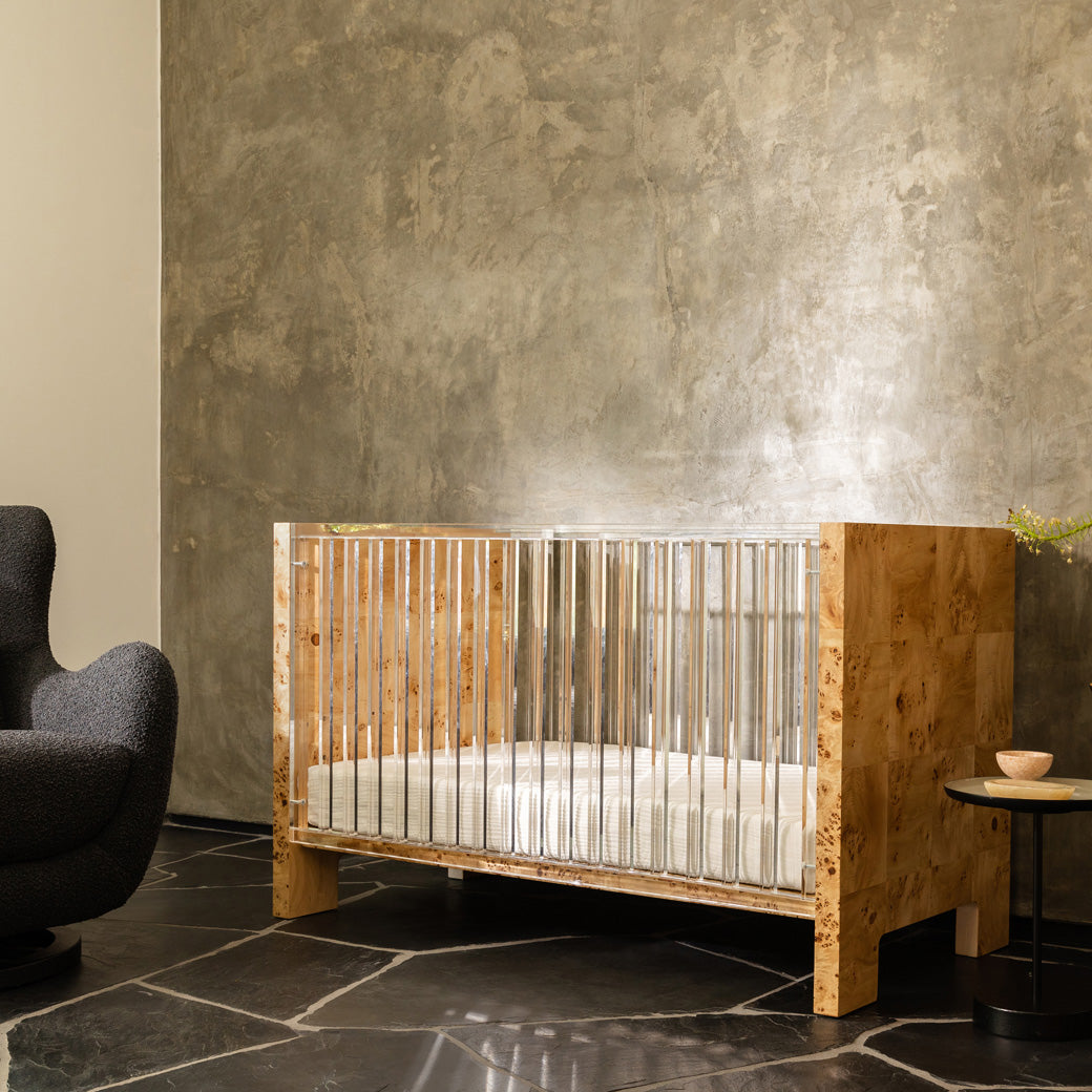 Nursery Works Altair Crib next to a recliner  in -- Color_Clear Acrylic with Burl