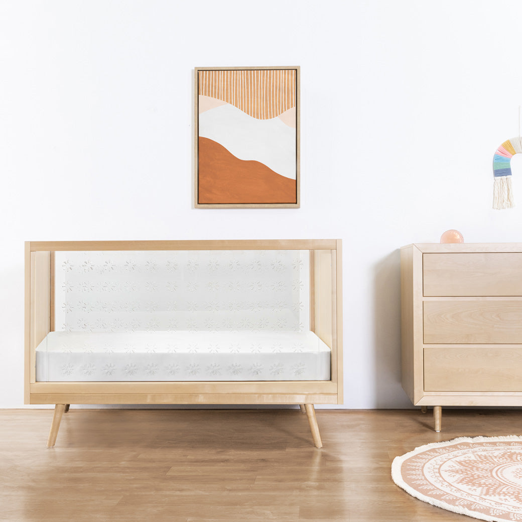 Ubabub Nifty Clear 3-in-1 Crib under a picture, next to a dresser  in -- Color_Natural Birch