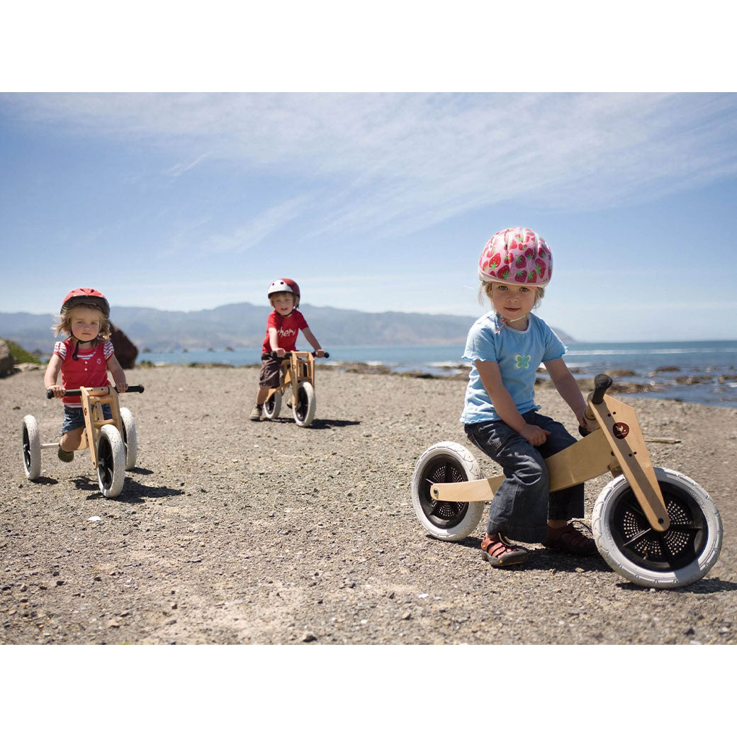 Three toddlers with helmets riding the Wishbone 3-in-1 Bike in -- Color_Natural