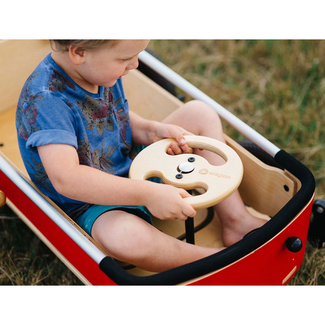 Toddler sitting at the wheel of the Wishbone Wagon in Red