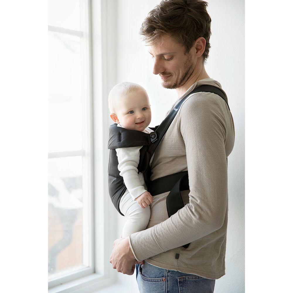 Side view of dad carrying baby in BABYBJÖRN Baby Carrier Mini in -- Color_Black Woven