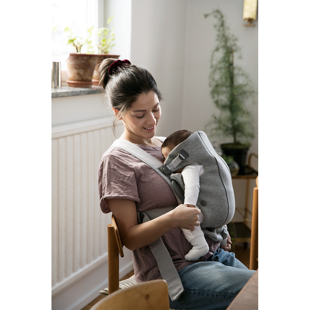 Mom sitting in chair with baby in BABYBJÖRN Baby Carrier Mini in -- Color_Light Gray 3D Jersey