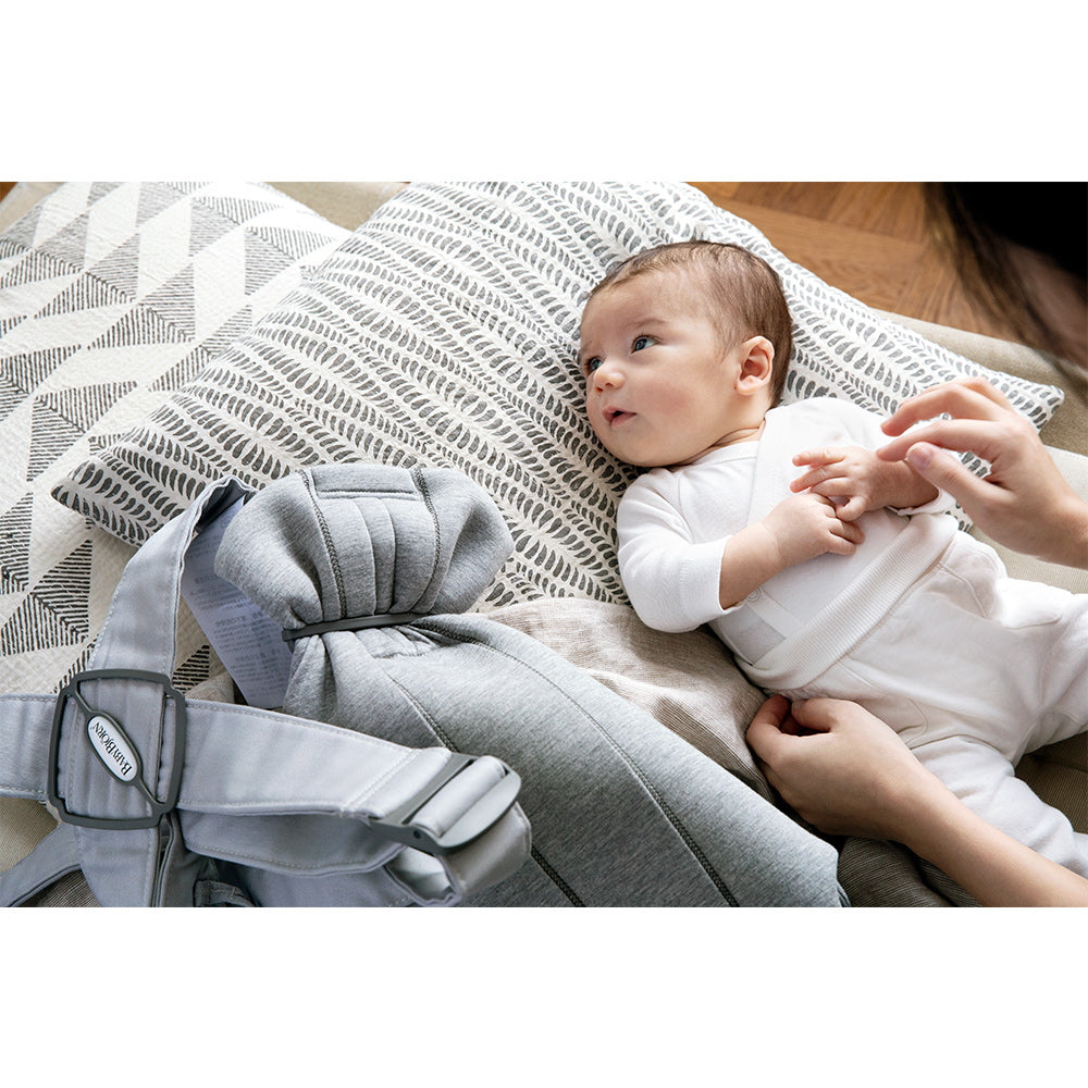 BABYBJÖRN Baby Carrier Mini next to laying baby in -- Color_Light Gray 3D Jersey