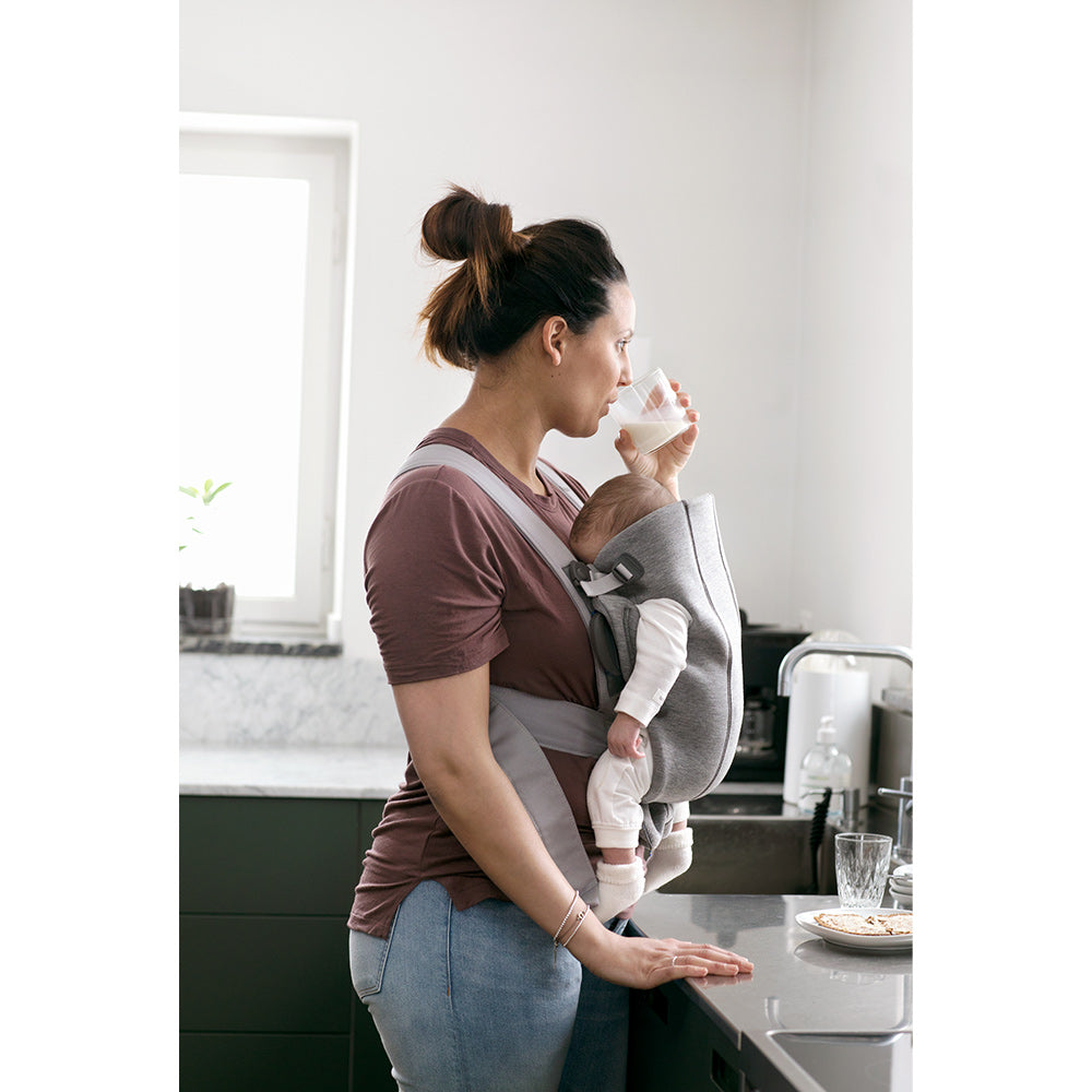 Side view of mom holding baby in BABYBJÖRN Baby Carrier Mini in -- Color_Light Gray 3D Jersey
