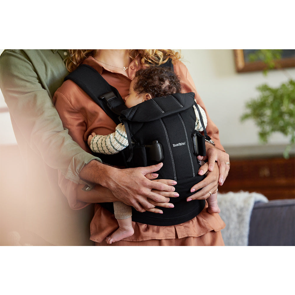 Mom and Dad holding baby in the BABYBJÖRN Baby Carrier One in -- Color_Black Woven Mix