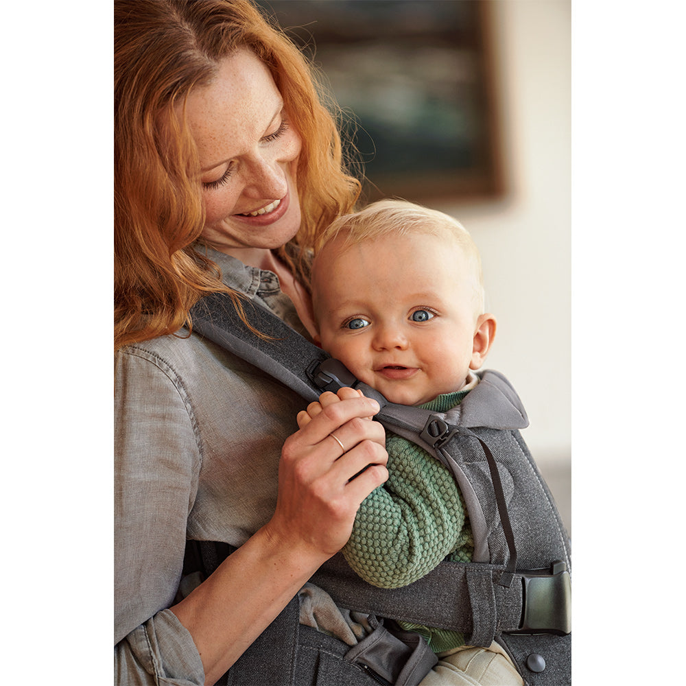 Side view of a happy baby in BABYBJÖRN Baby Carrier One in -- Color_Denim Gray/Dark Gray Woven Mix