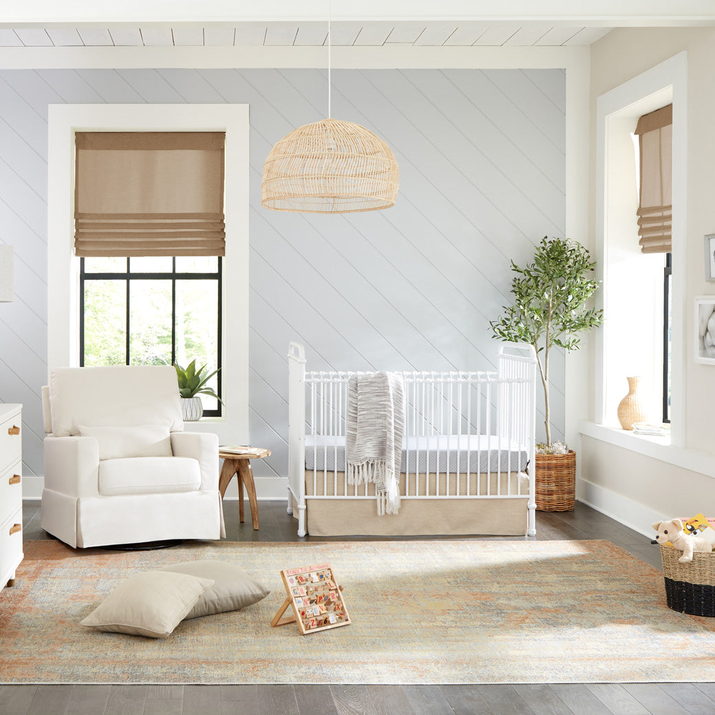 Namesake`s Abigail 3 in 1 Crib in a room next to a recliner, reading table, and plant  in -- Color_Washed White