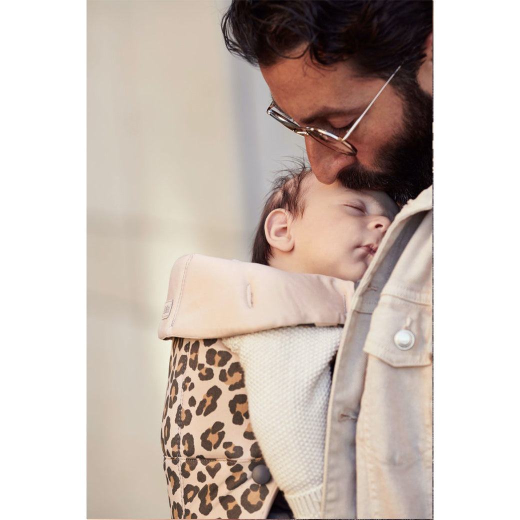 Dad kissing baby's forehead while baby sleeps in BABYBJÖRN Baby Carrier Mini in -- Color_Beige Leopard Cotton