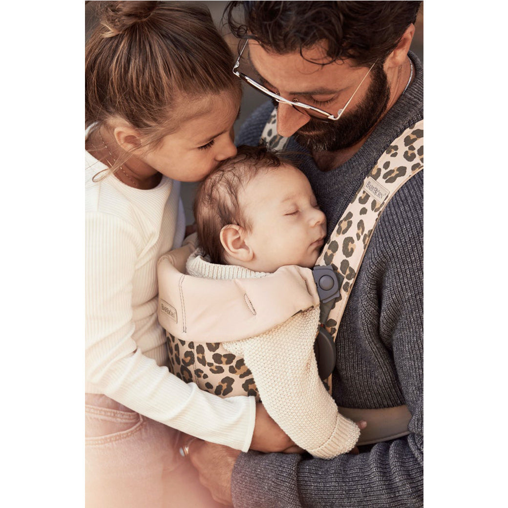 Little sister kissing baby being carried by dad in the BABYBJÖRN Baby Carrier Mini in -- Color_Beige Leopard Cotton