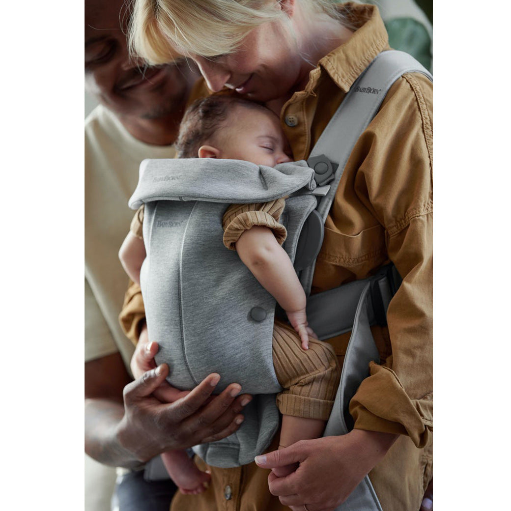 Mom carrying baby in BABYBJÖRN Baby Carrier Mini with dad next to them in -- Color_Light Gray 3D Jersey