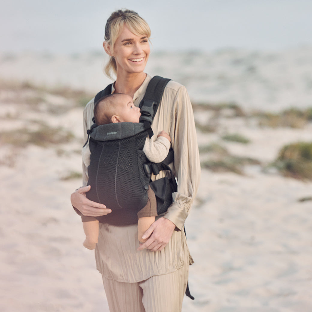 Mom at the beach carrying baby in Babybjorn Baby Carrier Harmony in -- Color_Black 3D Mesh