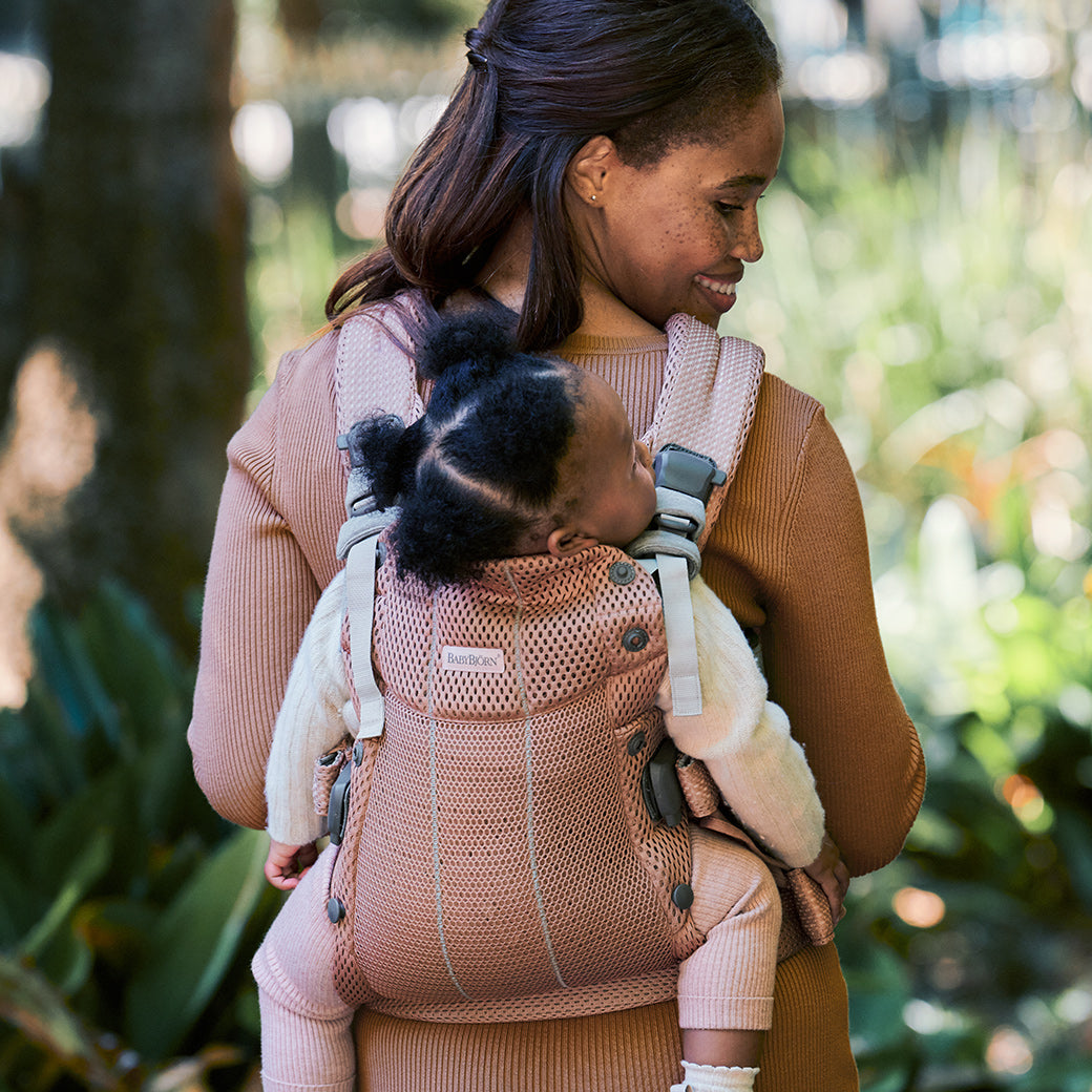 Mom carrying baby on back in the Babybjorn Baby Carrier Harmony in -- Color_Dusty Pink 3D Mesh