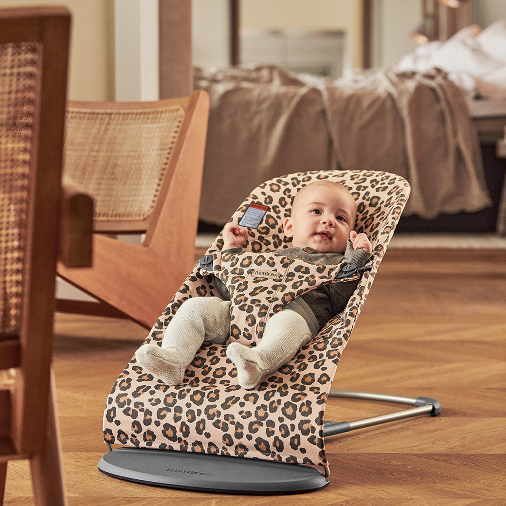 Baby in BABYBJÖRN Bouncer Bliss next to chairs in -- Color_Beige Leopard Classic Quilt Cotton