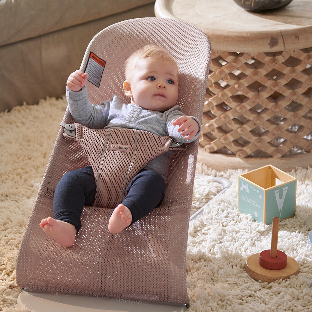 Baby in BABYBJÖRN Bouncer Bliss next to stacking toy  in -- Color_Dusty Pink Mesh