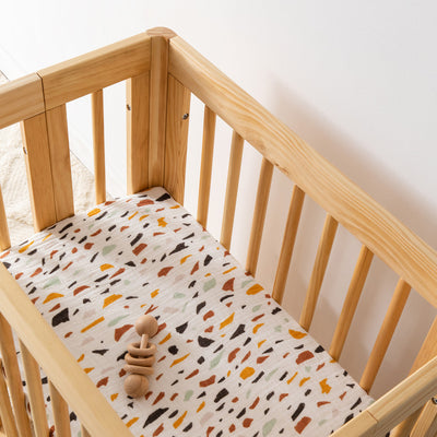 Babyletto All-Stages Bassinet Sheet In GOTS Certified Organic Muslin Cotton in a crib with a toy in -- Color_Terrazzo