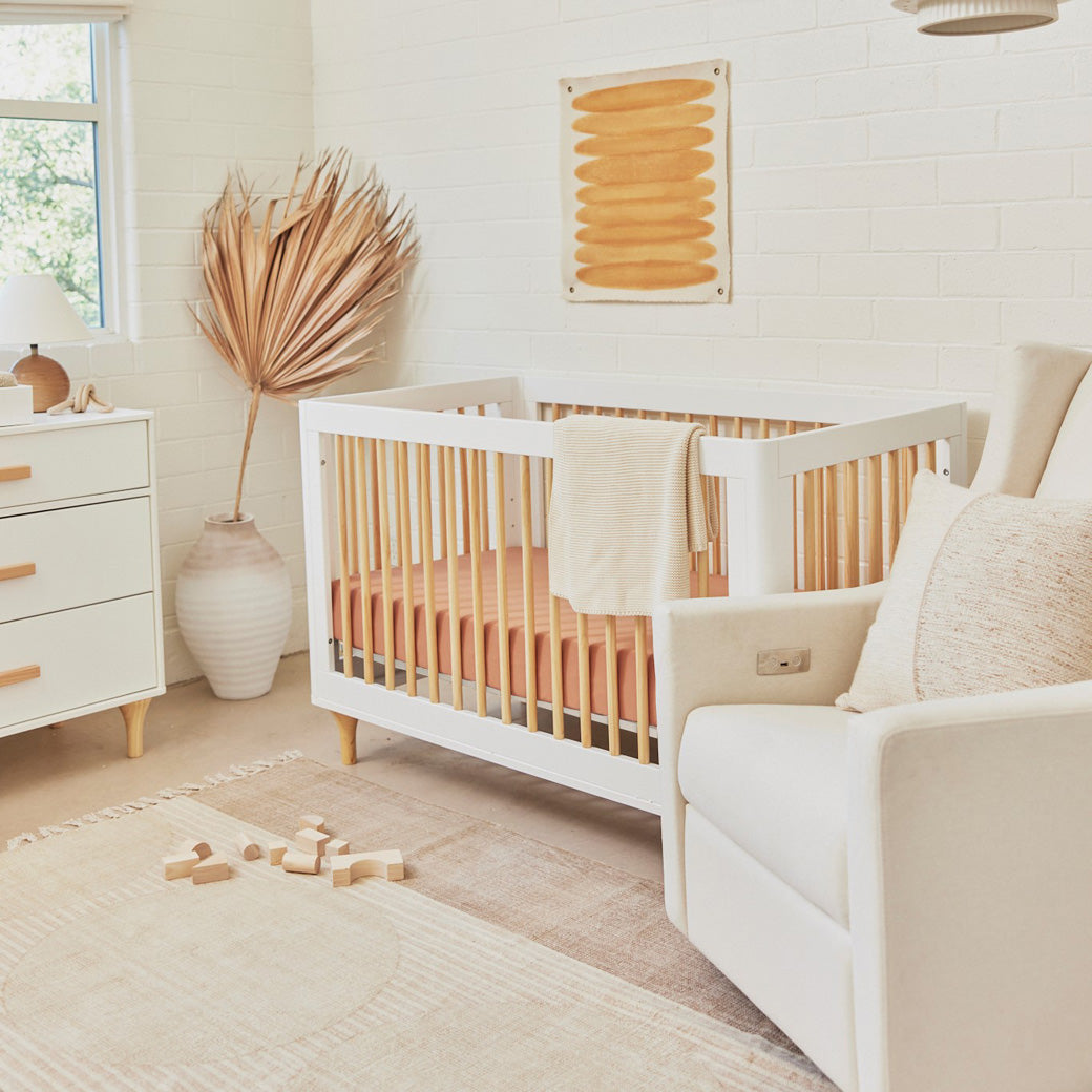 Babyletto Kiwi Glider Recliner next to a crib  in -- Color_Performance Cream Eco-Weave