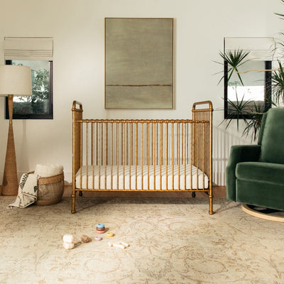 Namesake`s Abigail 3 in 1 Crib next to lamp and recliner  in -- Color_Vintage Gold