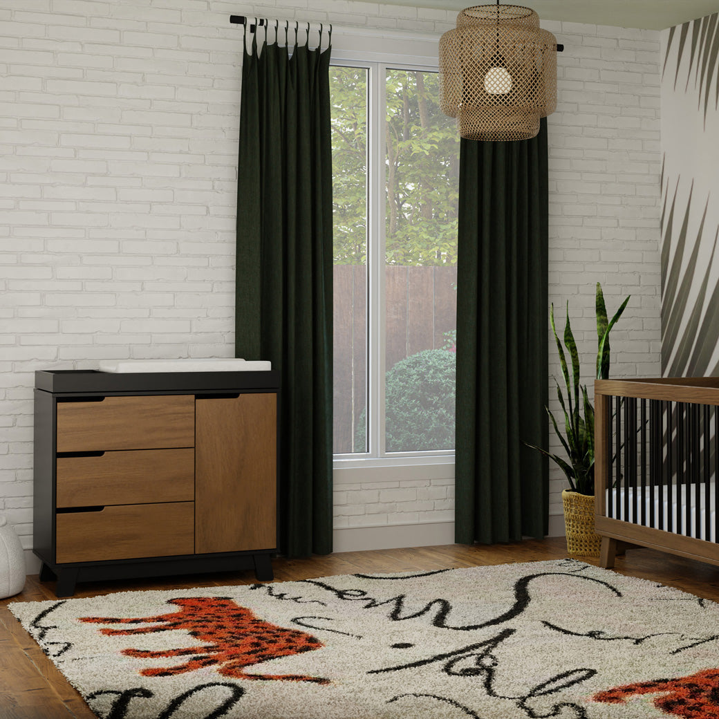 Lifestyle distance view of The Babyletto Hudson Changer Dresser next to window  in -- Color_Black/Natural Walnut