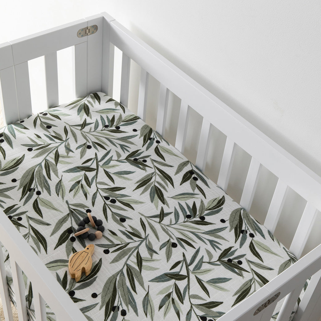 A crib with a toy inside  equipped with Babyletto's Mini Crib Sheet in -- Color_Olive Branches