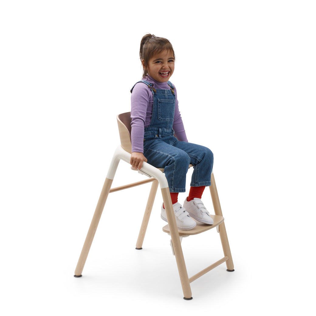 A child sitting in a Bugaboo Giraffe High Chair without the baby set in --Color_Neutral Wood / White