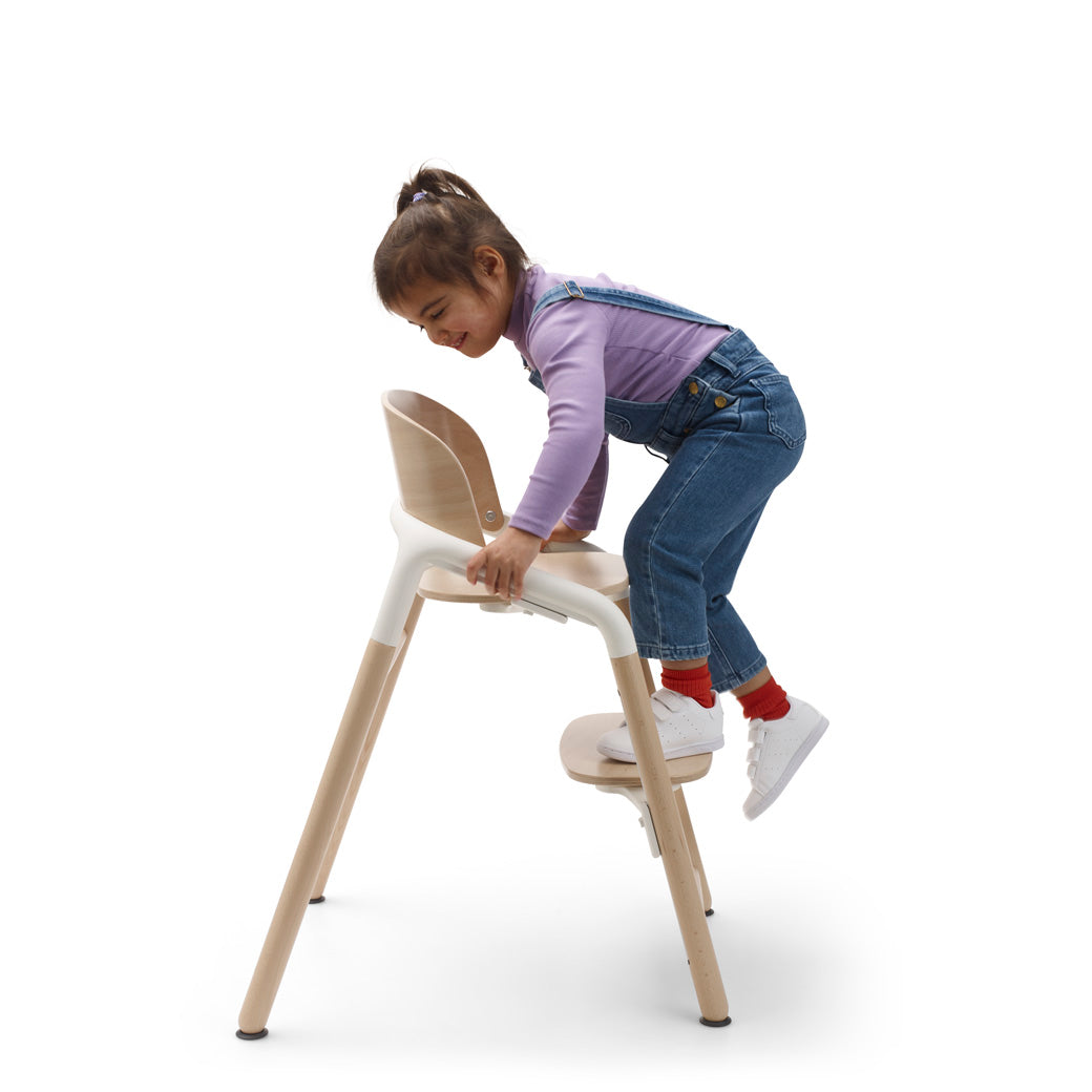 Child climbing onto the Bugaboo Giraffe High Chair in --Color_Neutral Wood / White