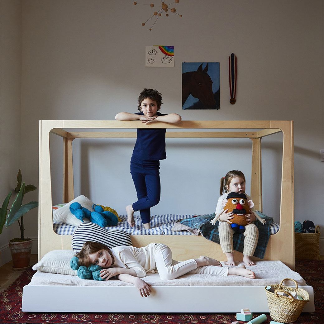 Lifestyle view of Oeuf Perch Nest Bed with a mattress in the middle and bellow, and three kids are on the bed