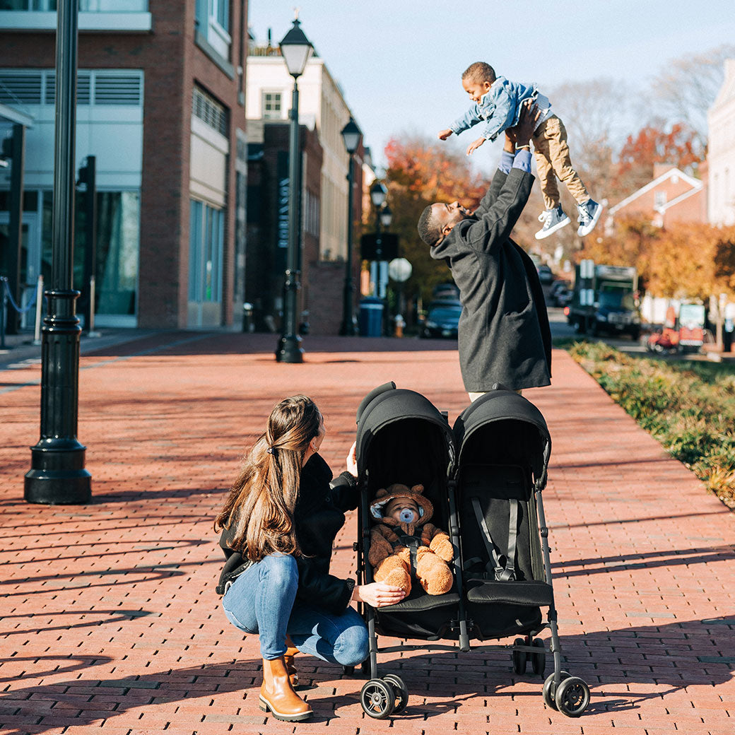 Father tossing his son in the air and mother crouched next to a baby in UPPAbaby G Link V2 Stroller in --Color_Jake