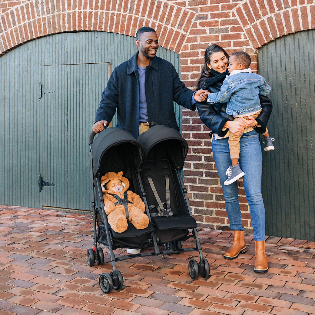 Mother holding a child and father holding the UPPAbaby G Link V2 Stroller with baby inside in --Color_Jake