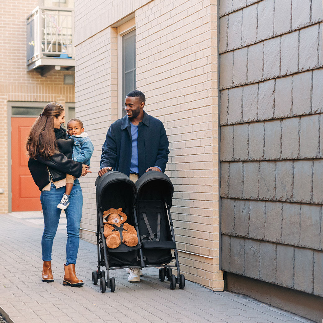 Mother holding a child and father pushing the UPPAbaby G Link V2 Stroller in --Color_Jake