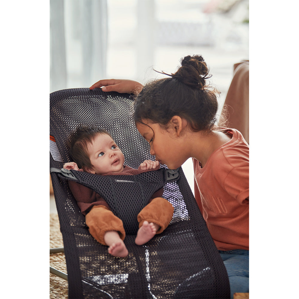 Sister kissing baby sitting in BABYBJÖRN Bouncer Bliss in -- Color_Anthracite (Slate Gray) Mesh